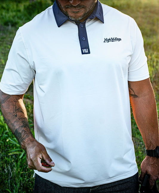 Person wearing a white polo shirt with a  'High Voltage' logo, and holding a drag up challenge coin in an outdoor setting