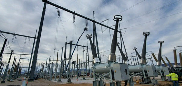 High-voltage electrical substation under construction with workers and cranes installing equipment and steel structures
