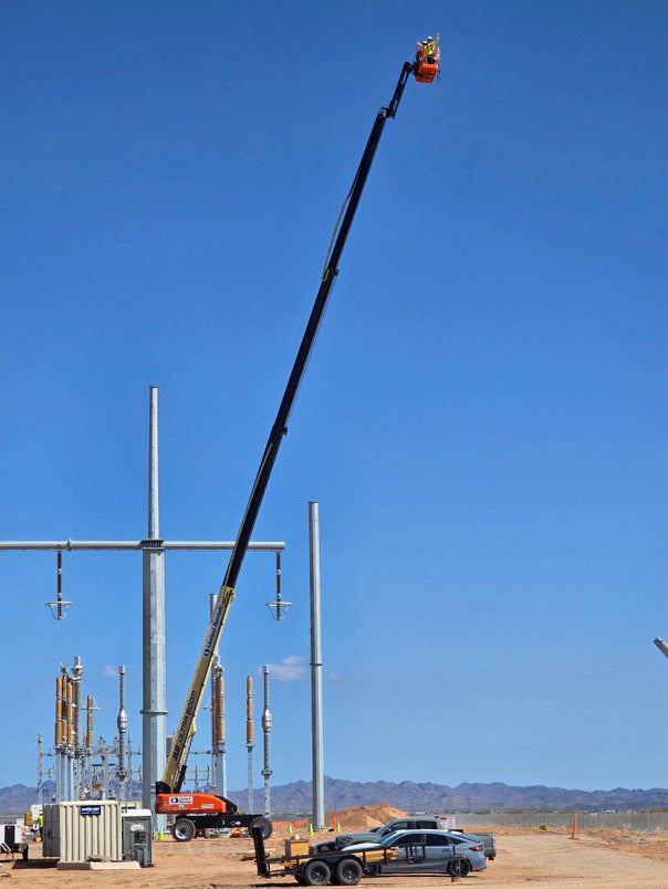 Substation workers elevated on a boom crane performing high-voltage substation installation at construction site