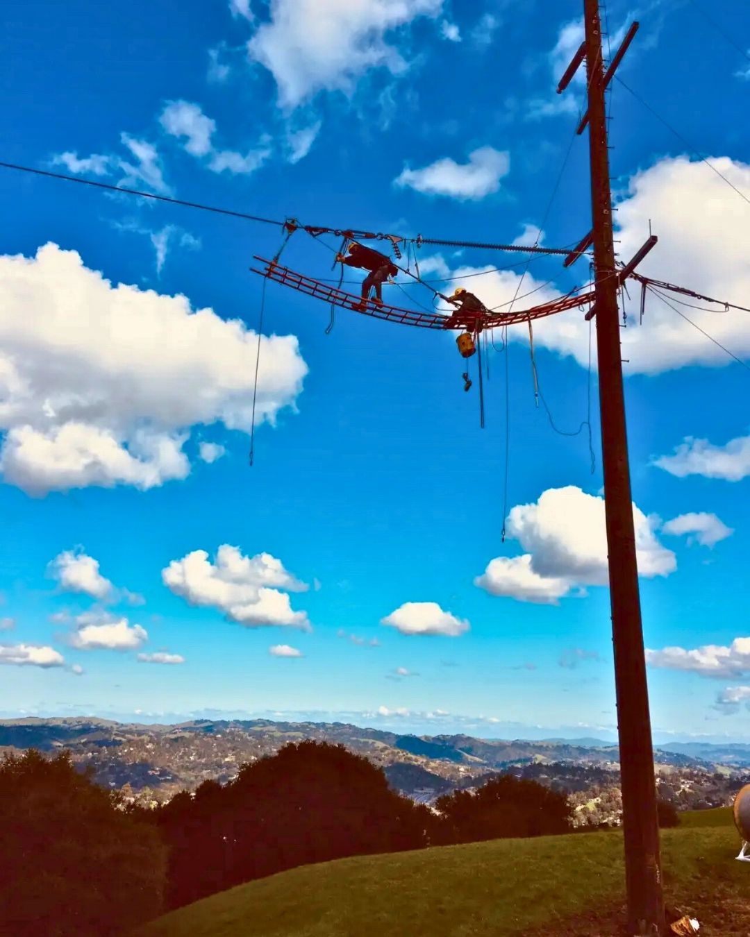 Two linemen repairing a high-voltage power line against a blue sky.
