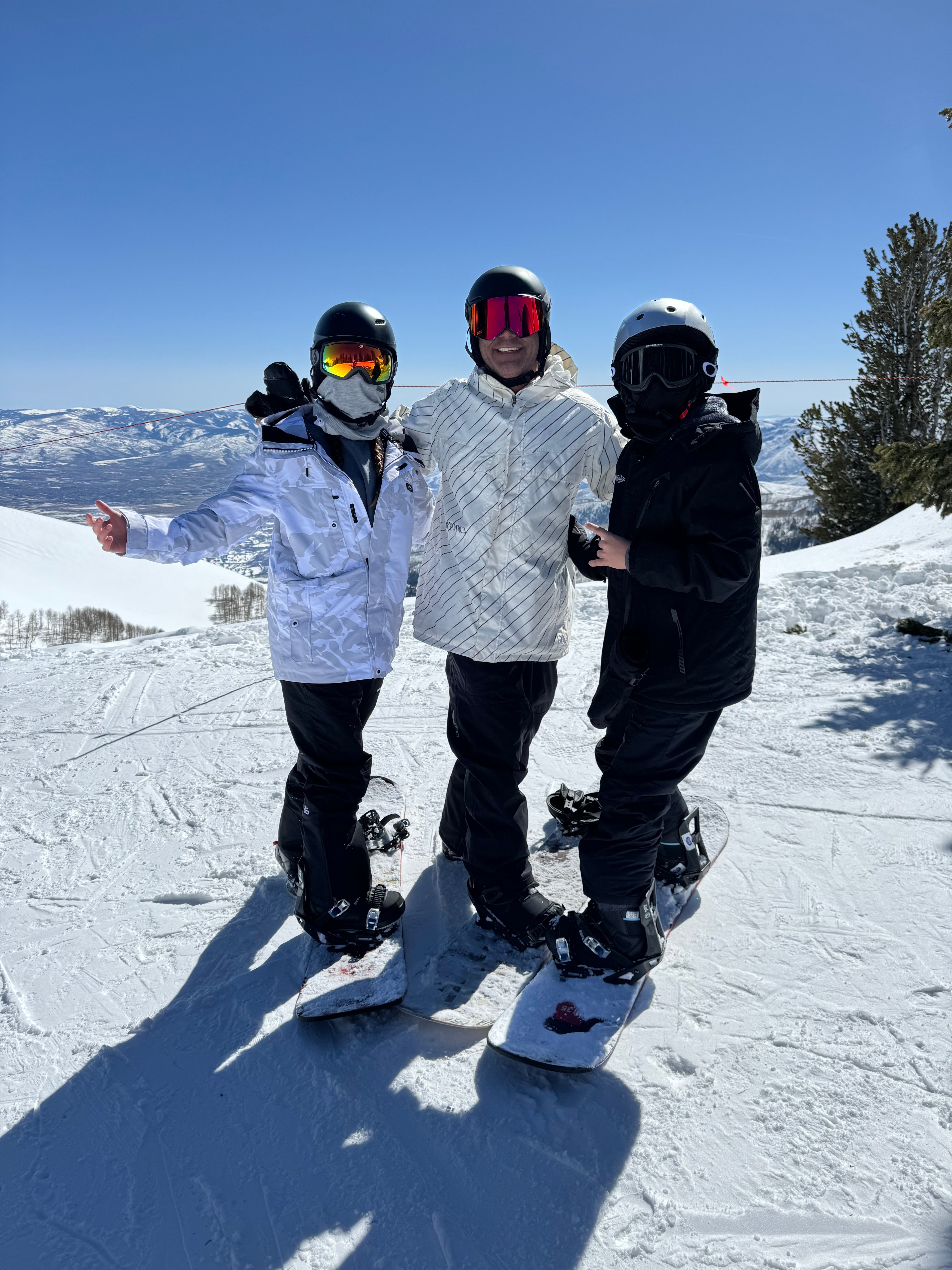 Three snowboarders posing on a snowy mountain slope under clear blue skies