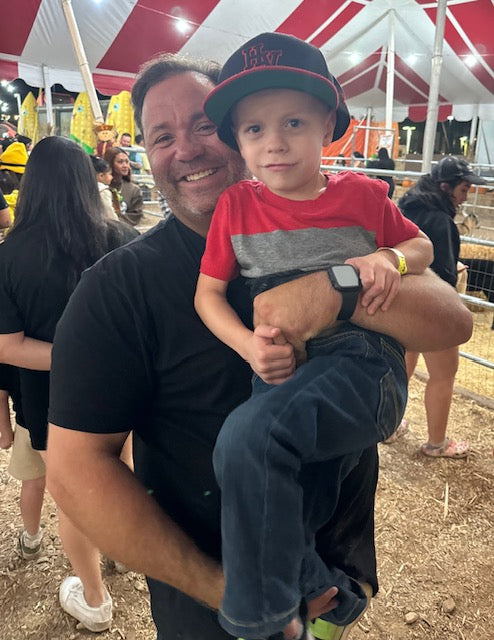Sammy Micco smiling and holding his son at a local fair.